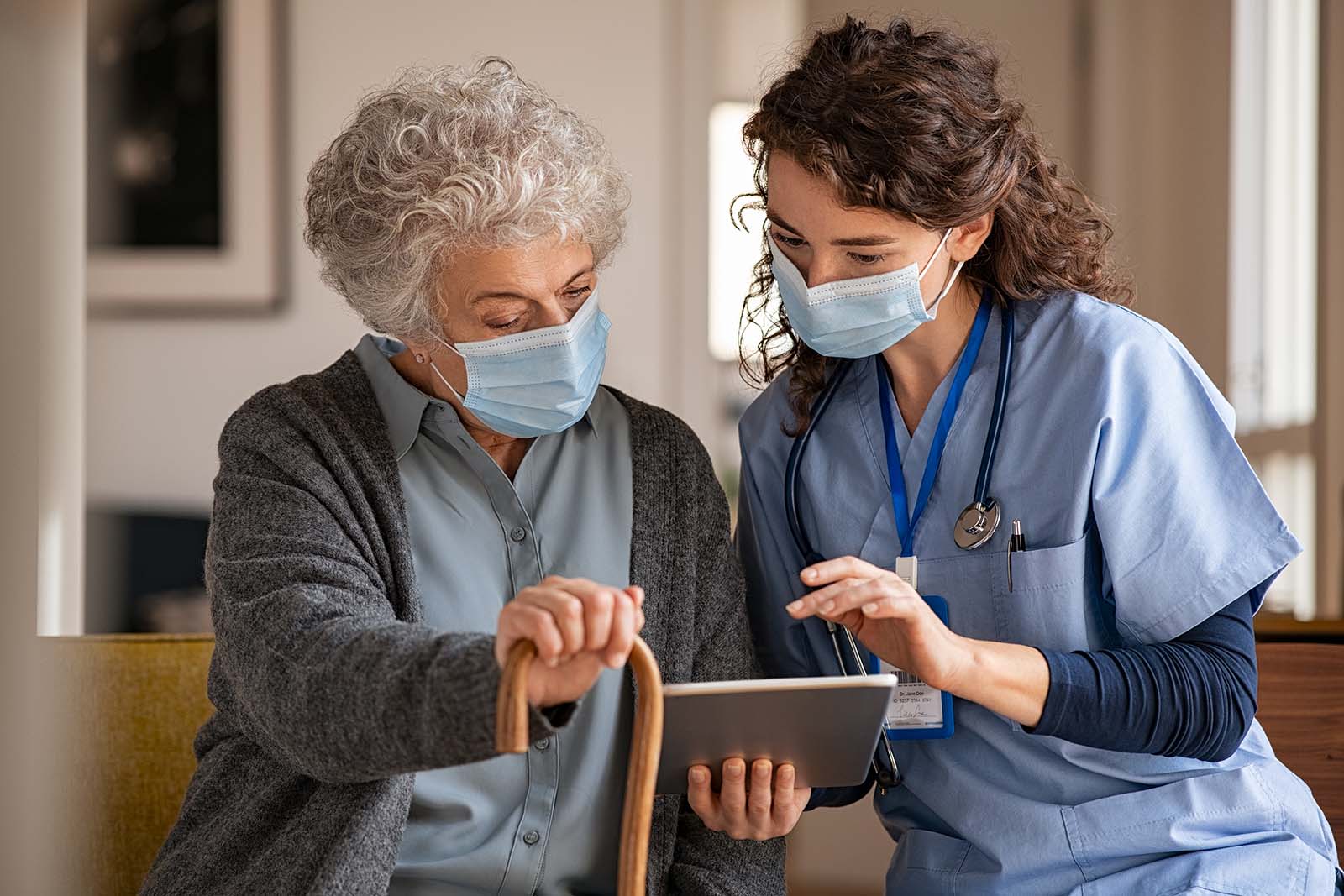 Masked elderly woman and nurse using tablet