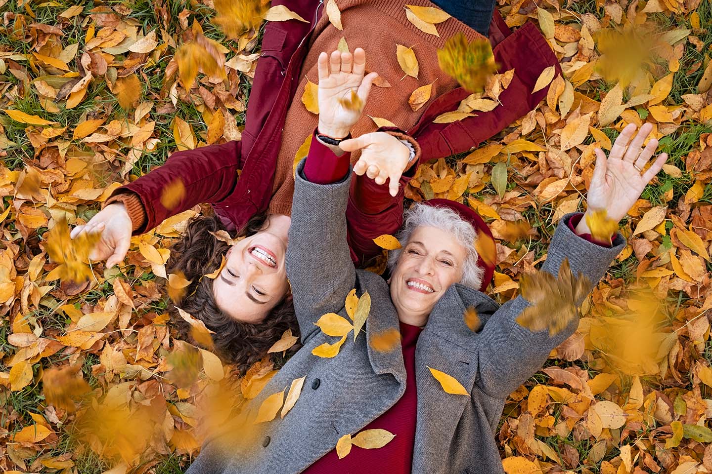 Elderly woman and younger woman laying in pile of leaves in autumn